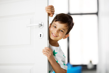 Fototapeta na wymiar childhood, fun and people concept - happy little boy behind door at home