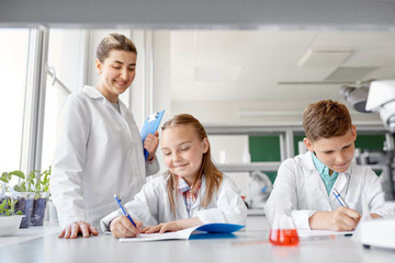 Fototapeta premium education, science and children concept - teacher and students studying chemistry at school laboratory and writing to workbooks