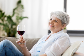 people, alcohol and leisure concept - happy smiling senior woman with glass of red wine at home