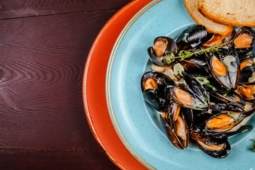 Boiled mussels in copper cooking dish on dark wooden background close up