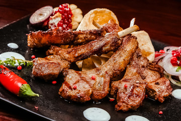 rack of lamb on a black plate decorated with pepper, pomegranate, onion and garlic