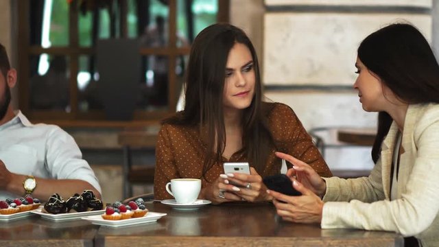 One-on-one meeting.Two young business women sitting at table in cafe.Girl shows her friend image on screen of smartphone. On table is closed notebook.Meeting friends.