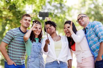 people, friendship and international concept - happy smiling young woman and group of happy friends taking picture by selfie stick in park