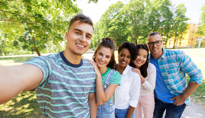 people, friendship and international concept - happy smiling young woman and group of happy friends taking selfie outdoors