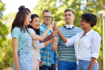 success, friendship and international concept - group of happy smiling friends making thumbs up gesture in park