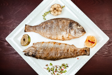 Fried fish on a wooden background. With lemons and spices.