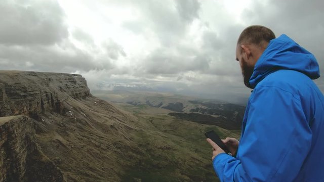 bearded hipster man takes pictures on his smartphone while on the rocks in the mountains of the Caucasus