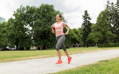 fitness, sport and healthy lifestyle concept - smiling woman with earphones running at park and...