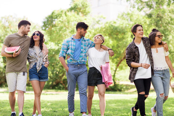 friendship and leisure concept - group of happy friends with picnic blanket and watermelon walking at summer park