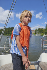 Fototapeta premium Child boy holding a yacht rudder. Cute boy captain on board of sailing yacht on summer cruise. Travel adventure, yachting with child on family vacation.