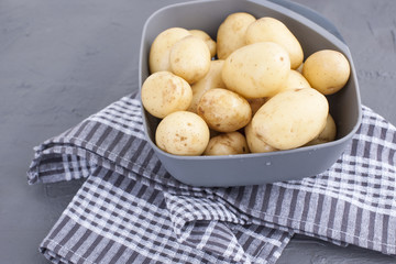 Young clean potatoes in a bowl on the table and a kitchen towel. Copy space.