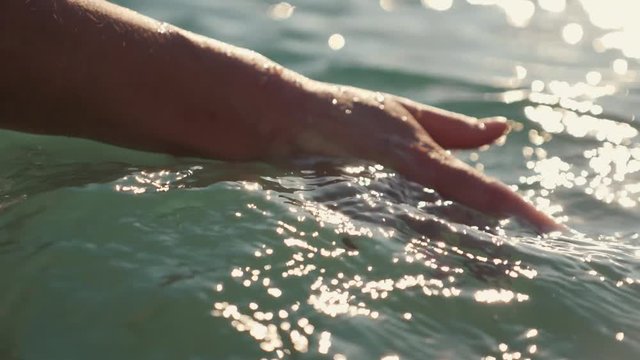 Female hand close-up in the sea. A girl stroking the sea waves