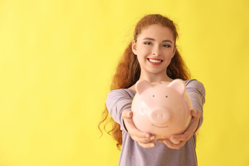 Young woman holding piggy bank on color background. Money savings concept