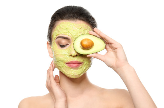 Beautiful young woman with facial mask and fresh avocado on white background