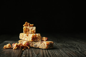 Different grain cereal bars on wooden table against black background. Healthy snack
