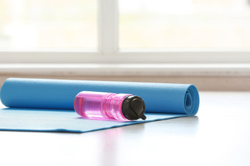 Yoga mat and bottle of water on wooden floor