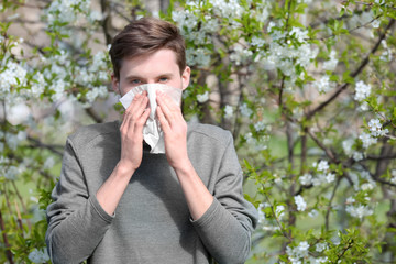 Young man with nose wiper near blooming tree. Allergy concept