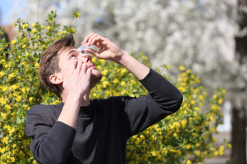 Young man using eye drops near blooming tree. Allergy concept