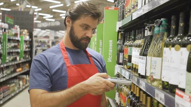 supermarket employee in red aport scanning barcode at wine section in supermarket