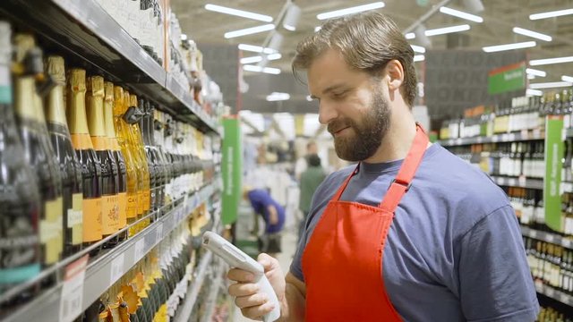 Sales clerk in red aport scanning barcode at wine section in supermarket
