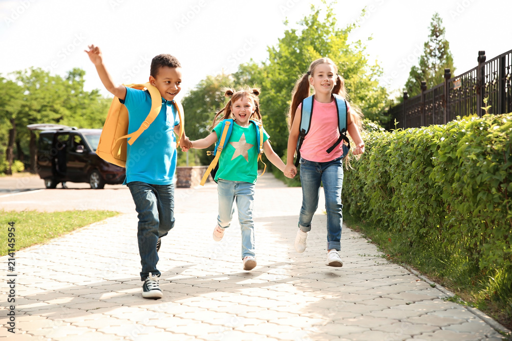 Poster Cute little children with backpacks running outdoors. Elementary school