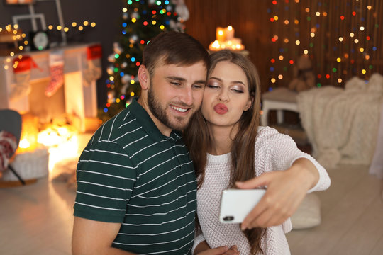 Happy young couple taking selfie in decorated for Christmas room