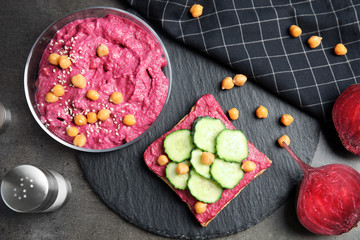 Flat lay composition with bowl of beet hummus, toast bread and cucumber on dark background