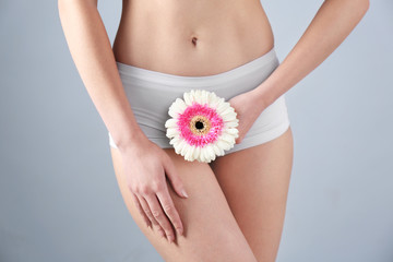 Young woman holding flower near underwear on grey background. Gynecology