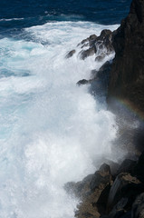 Rainbow between breaking waves in rocky coast