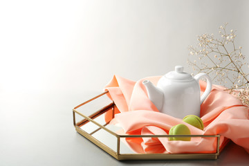 Tray with teapot and macarons on light background