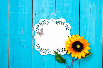 Blank wood sign with floral border butterfly and sunflower hanging on antique rustic teal blue wooden door; message board with copy space