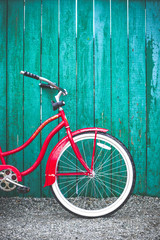 Red women's retro style bicycle leaning against a bright blue green wooden fence.