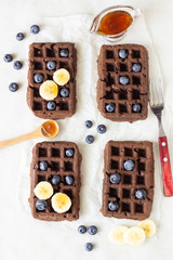 Chocolate belgian waffles with fresh blueberries, banana and honey on a white paper.