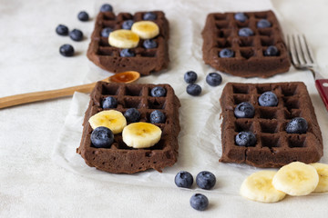 Chocolate belgian waffles with fresh blueberries, banana and honey on a white paper.