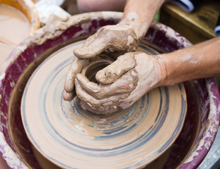 Potter's hands and the child's hand in clay over a potter's wheel. A master class on production of pottery. Modeling of clay on a potter's wheel