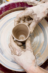 Potter's hands and the child's hand in clay over a potter's wheel. A master class on production of pottery. Modeling of clay on a potter's wheel