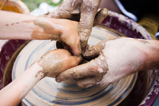Potter's hands and the child's hand in clay over a potter's wheel. A master class on production of pottery. Modeling of clay on a potter's wheel