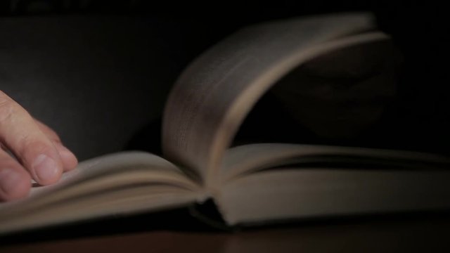 Close-up of a man's hand holding an open paper book, turning the pages with his fingers