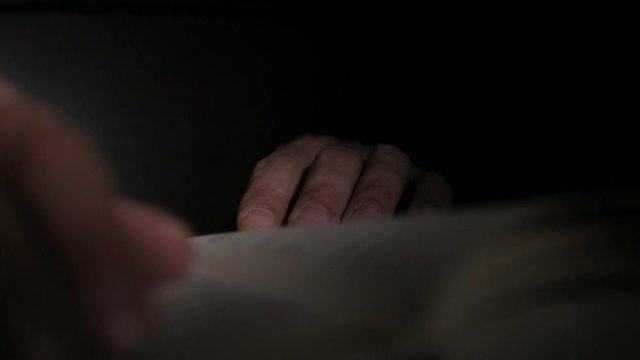 Close-up of a man's hand holding an open paper book, turning the pages with his fingers