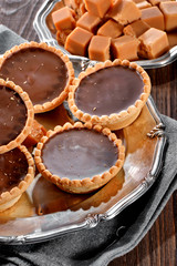 tartlets with chocolate filling close-up and toffee caramel pieces on silver vintage plate decorated with linen napkin on wooden table background

