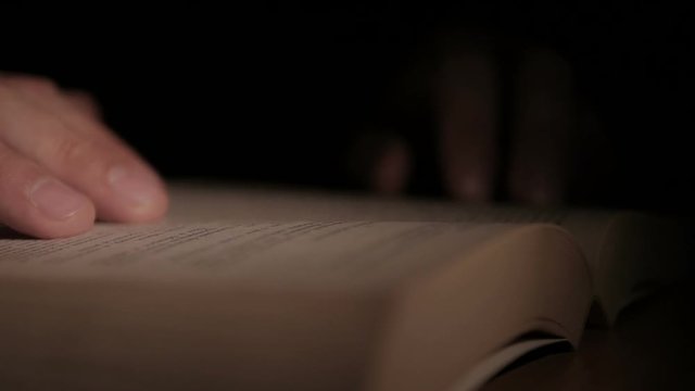 Close-up of a man's hand holding an open paper book, turning the pages with his fingers