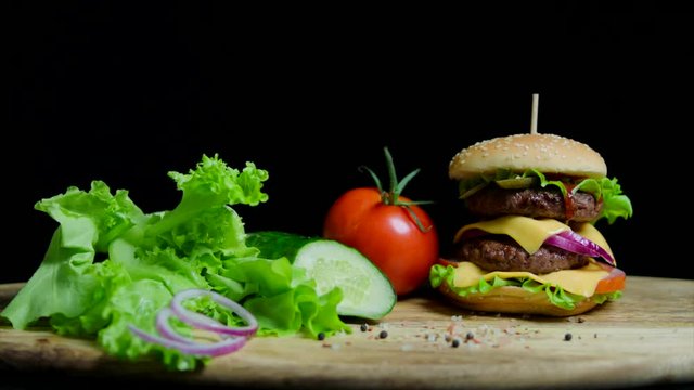 Fresh vegetables and tasty burger with cheese and beef cutlets on the black background