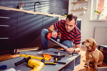 Man with dog checking blueprints while building kitchen cabinets