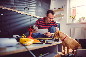 Man with dog checking blueprints while building kitchen cabinets