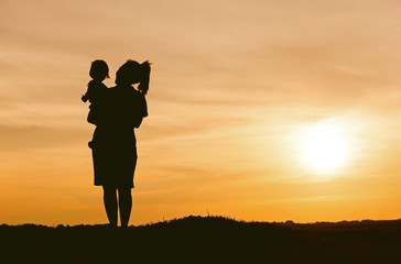 Silhouette of mother and daughter lifting child in air over scenic sunset sky at riverside. relaxation time and happiness