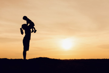 Silhouette of mother and daughter lifting child in air over scenic sunset sky at riverside....