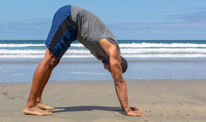 Athletic man at the beach in Downward-Facing Dog yoga pose