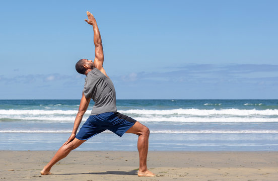Athletic man at the beach in Reverse Warrior yoga pose