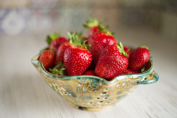 Fresh strawberries in a beautiful ceramic colander on a kitchen table