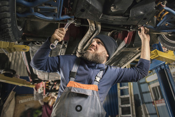 A bearded car mechanic works in the garage. Car mechanic in the garage. Hard work.